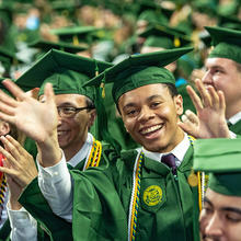 Graduates in a crowd wave to the camera